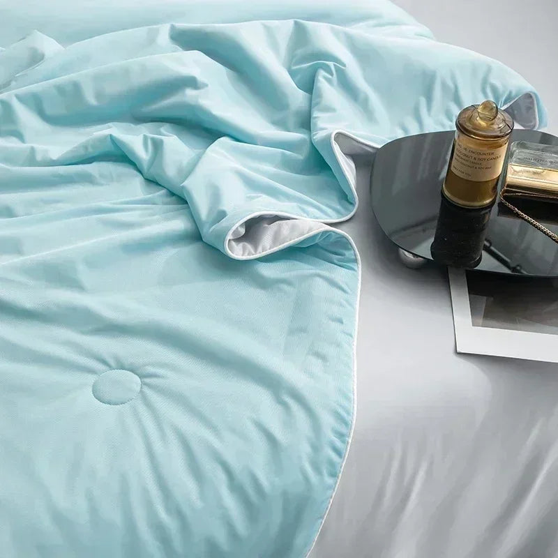 Light blue comforter on a bed with a bottle and book on a nightstand.