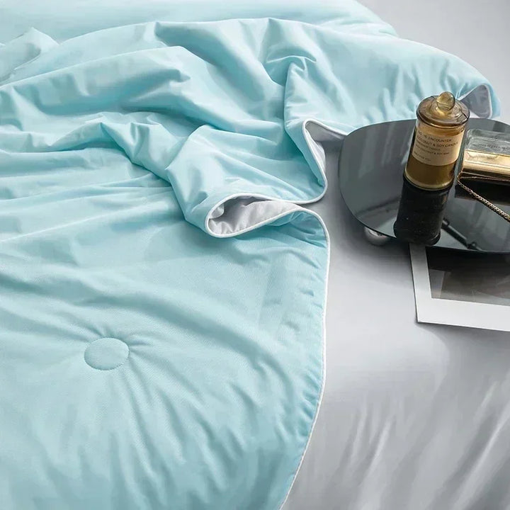 Light blue comforter on a bed with a bottle and book on a nightstand.